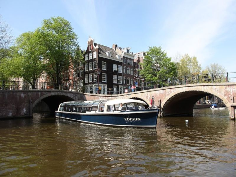 Glasboot fährt unter einer Steinbrücke durch eine Amsterdamer Gracht